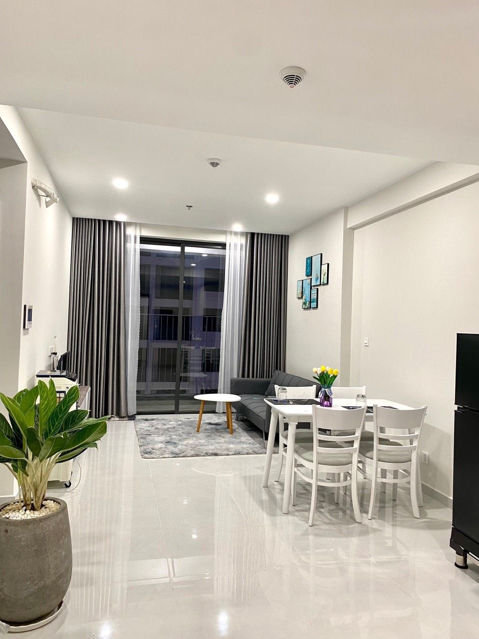 A modern living room with a dining area, a large window with curtains, and a flat-screen TV.