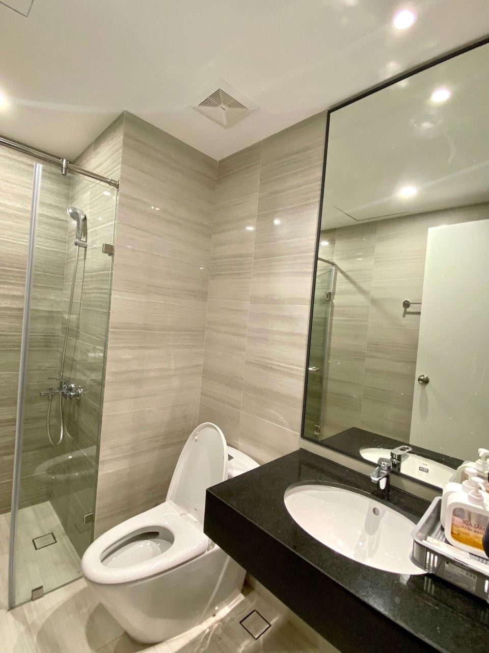 A modern bathroom with a glass-enclosed shower, a white toilet, and a black sink with a large mirror above it.
