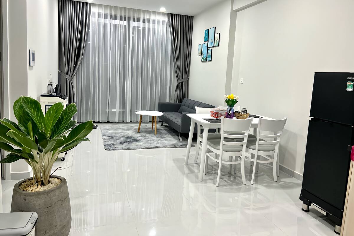 A modern living room with a sofa, dining table, chairs, a potted plant, and a refrigerator.