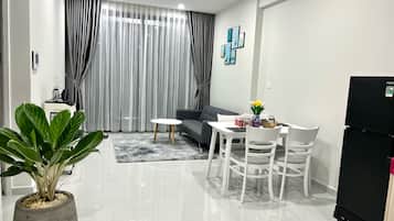 A modern living room with a sofa, dining table, chairs, a potted plant, and a refrigerator.