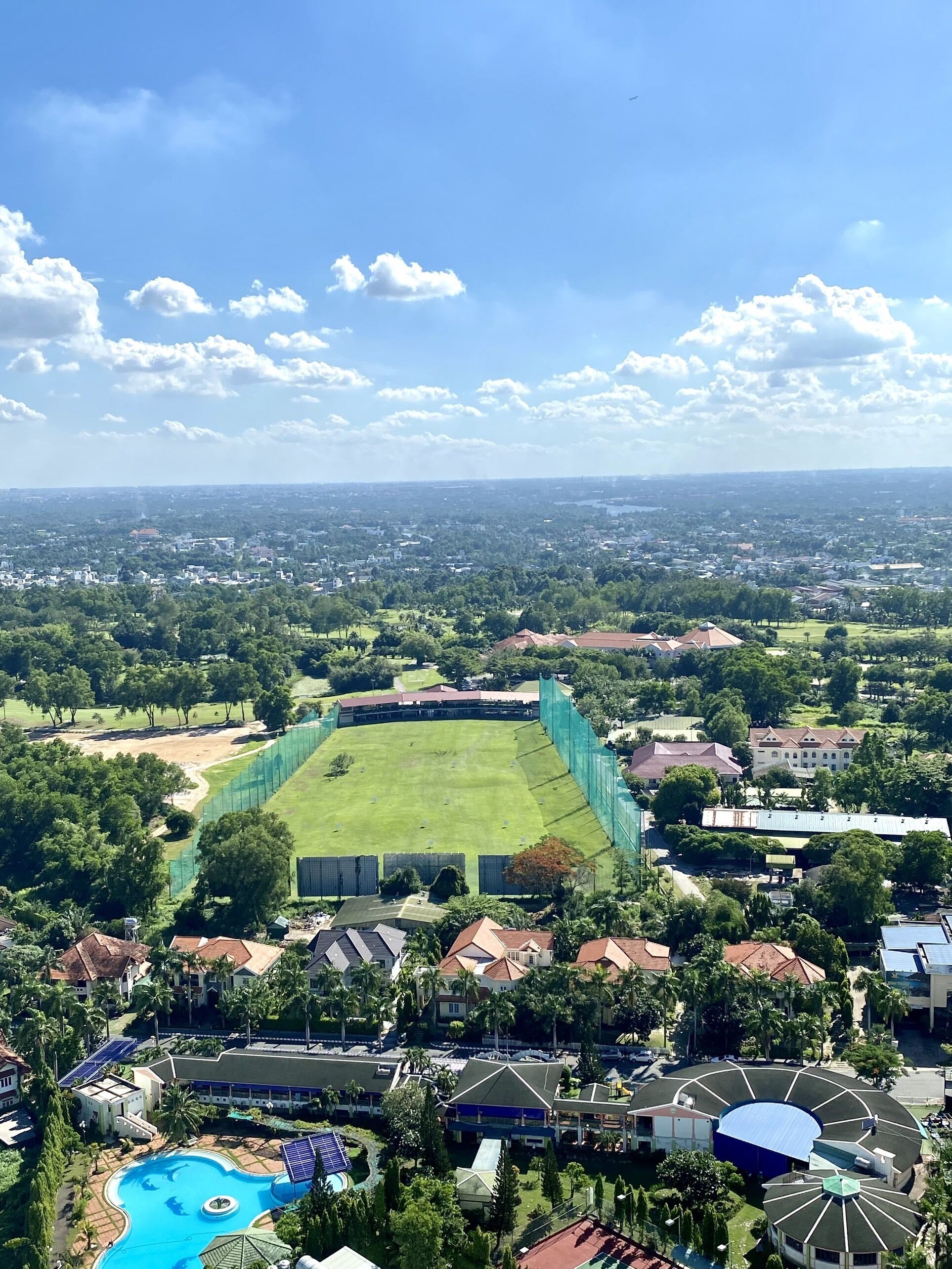 An aerial view of a resort with a large green field, a swimming pool, and surrounding residential buildings.