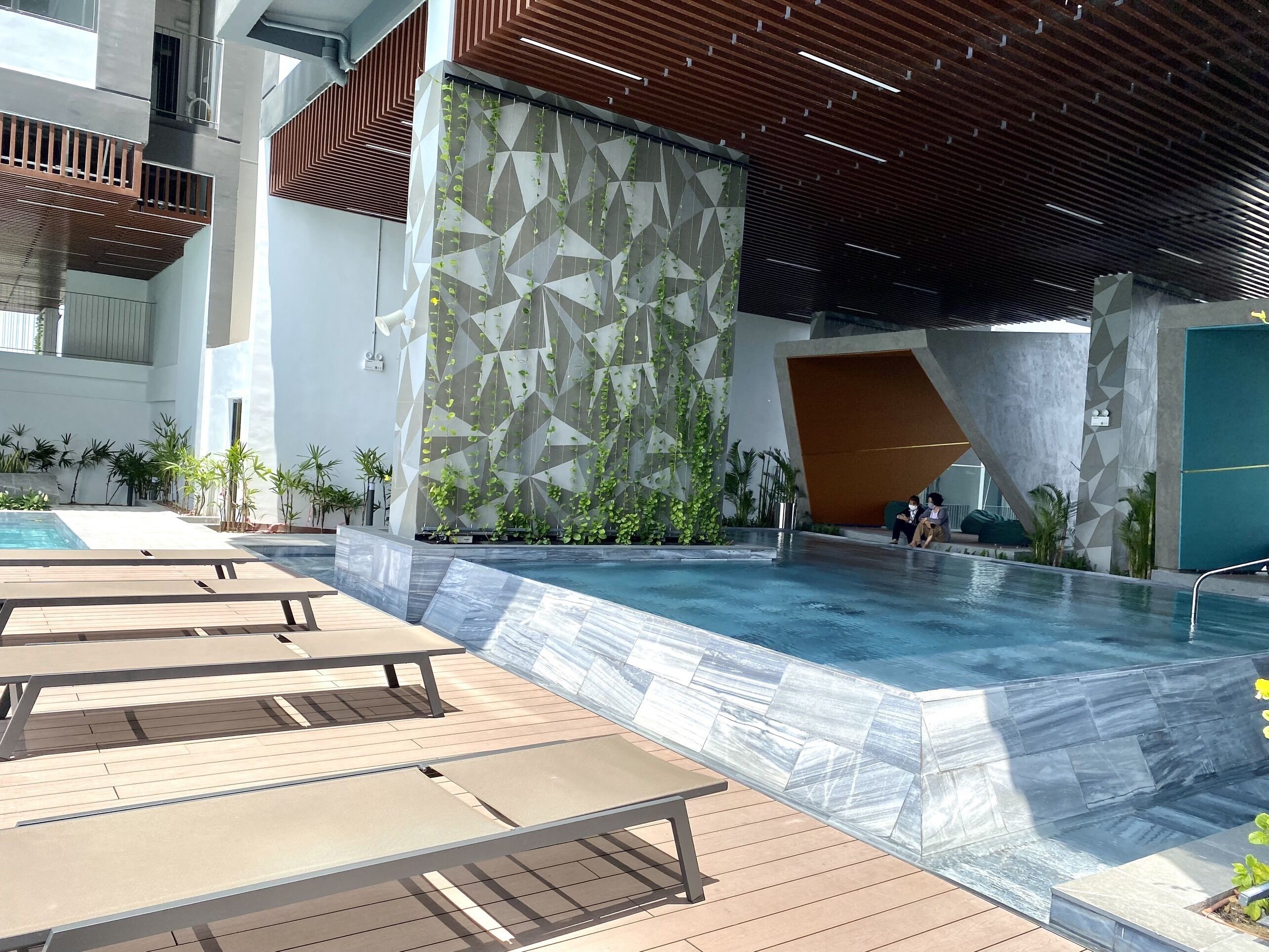 A modern indoor pool area with a geometric wall design, wooden deck seating, and a clear pool.