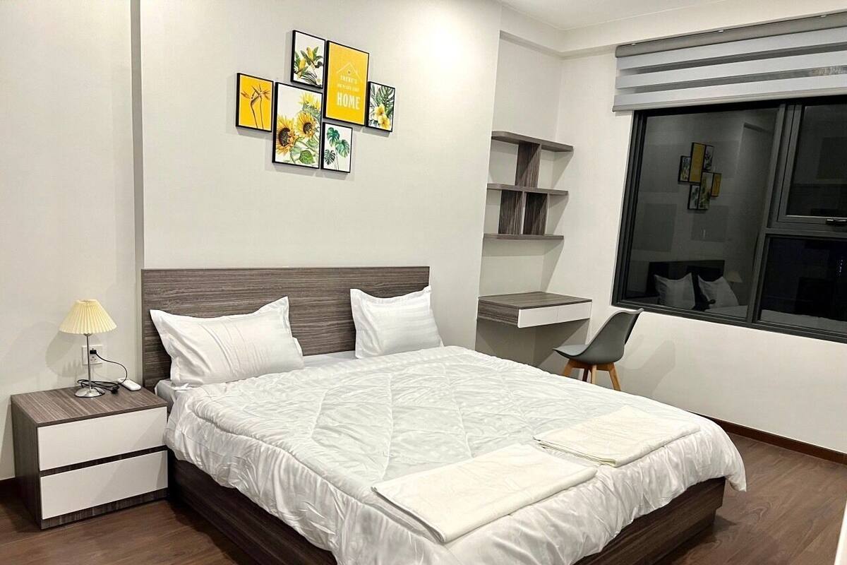 A modern bedroom with a large bed, bedside tables, a desk, and a chair.