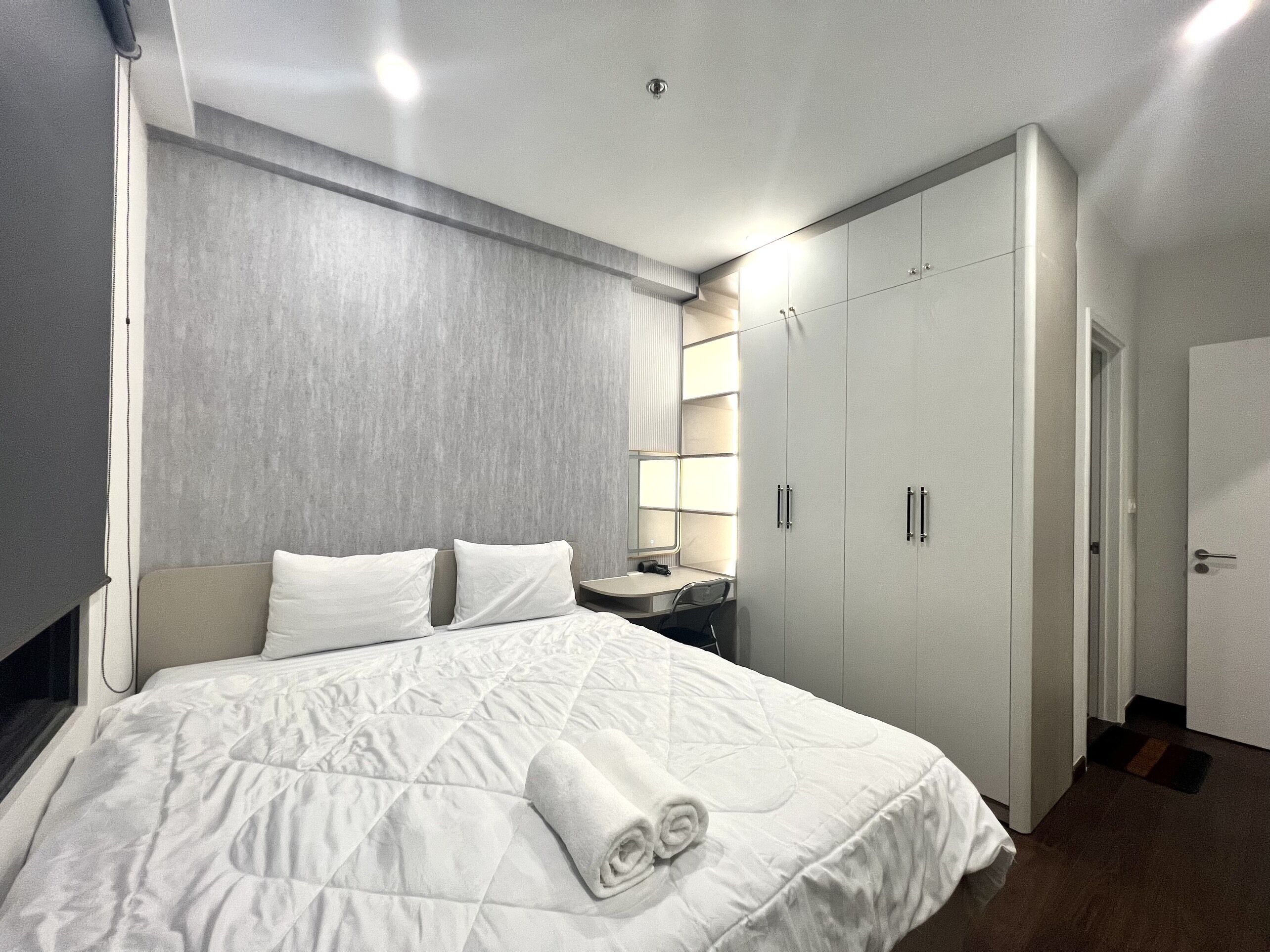A hotel room with a large bed, a desk, a wardrobe, and a mirror.