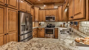 A kitchen with wooden cabinets, stainless steel appliances, a granite countertop, and a bowl of bread. - North Georgia Hideaway | Ellijay, GA (Ellijay)