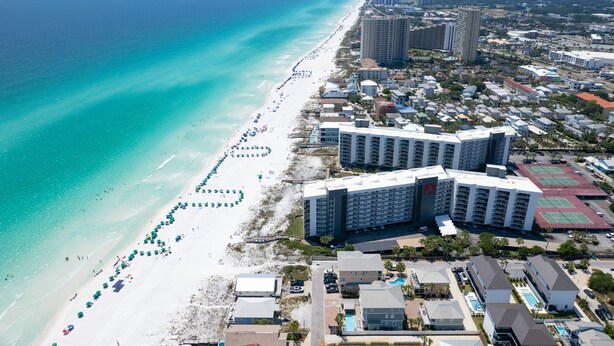 Eine Luftaufnahme einer Küstenregion mit einem Strand, gesäumt von Sonnenschirmen, und einer Reihe hoher Hotelgebäude.