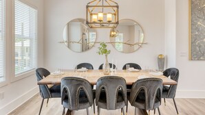 Ein Esszimmer mit einem Holztisch, sechs Polsterstühlen, einer Deckenleuchte und an Wänden befestigten Spiegeln.