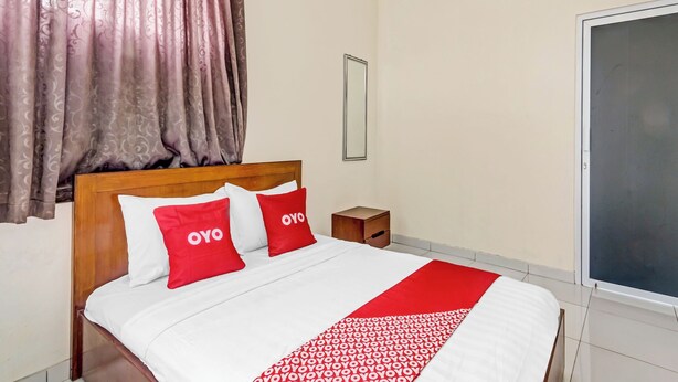 Een netjes opgemaakt bed met witrood beddengoed, een houten hoofdbord en een rood decoratief kleed.