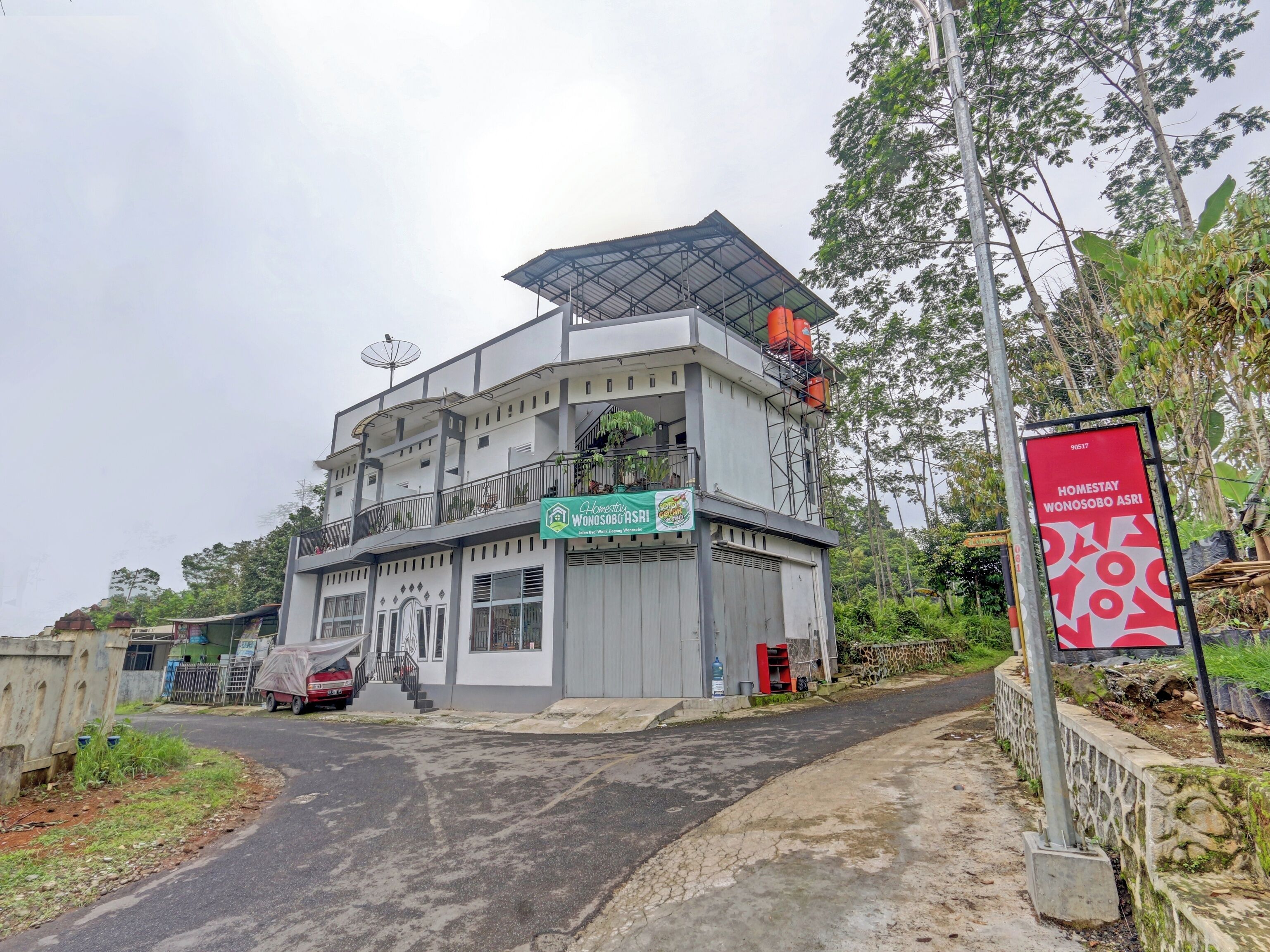 A multi-story building with a flat roof, a satellite dish, and a sign indicating it is a homestay.