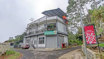 A multi-story building with a flat roof, a satellite dish, and a sign indicating it is a homestay.