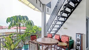 A balcony with a wooden table and chairs, potted plants, and a staircase. - OYO 90517 Homestay Wonosobo Asri (Wonosobo)
