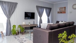 En moderne stue med sofa, fladskærms-tv, sofabord og en plante.