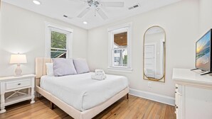 Une chambre à coucher comprenant un lit, des tables de chevet, une lampe, un ventilateur de plafond, un grand miroir et un téléviseur.