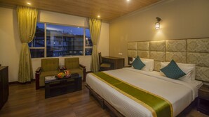 A hotel room with a large bed, a desk, a chair, and a view of the city at dusk. - NRS KINGSTON (Gangtok)