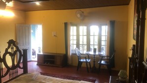 A room with a bed, a table, chairs, a fan, and a window with curtains. - Manikkal Bungalow Uphill Cottage Large (Mananthavady)