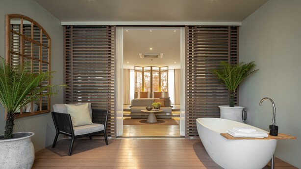 A modern bathroom with a freestanding bathtub, a seating area with a sofa and coffee table, and two potted plants. - Stay Plus Hotel Bangkok (Bangkok)