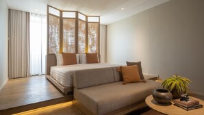 A modern bedroom with a large bed, a sofa, a small table with a plant and books, and a view through a window with curtains. - Stay Plus Hotel Bangkok (Bangkok)