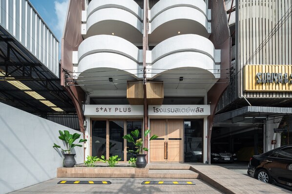 A hotel entrance with a covered walkway, potted plants, and a sign in both English and another language. - Stay Plus Hotel Bangkok (Bangkok)