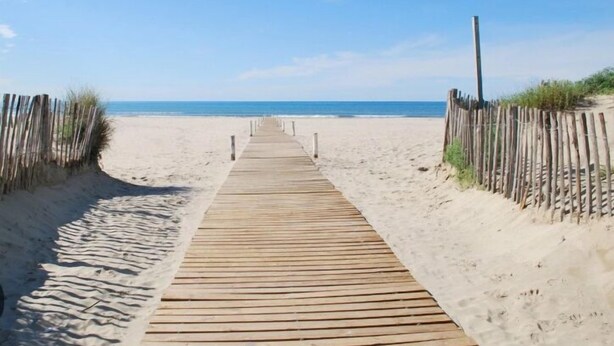 A wooden boardwalk leading to a sandy beach with a clear sky.