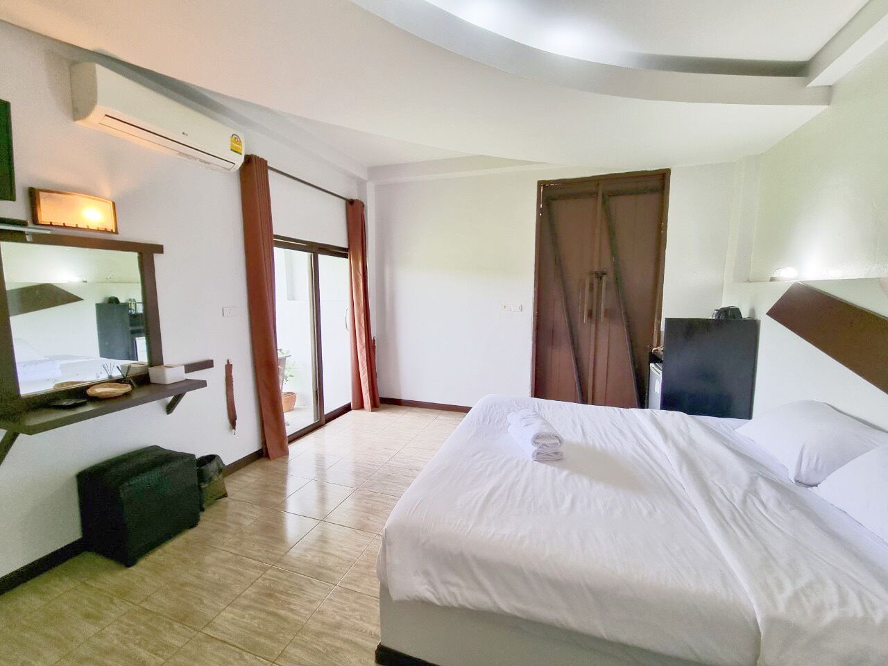 Une chambre d’hôtel comprenant un lit, un bureau avec un ordinateur, une chaise, une armoire et une porte-fenêtre coulissante donnant sur l’extérieur.