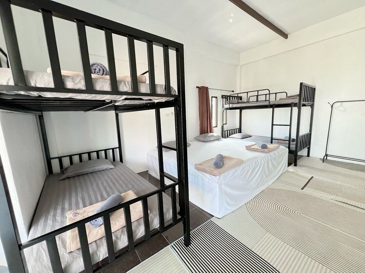 A dormitory-style room with bunk beds, a white bedspread, and a patterned rug.