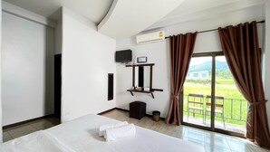 Ein Hotelzimmer mit einem großen Bett, einem an der Wand befestigten Fernseher, einer Klimaanlage und einem Balkon mit Blick auf Grünflächen.