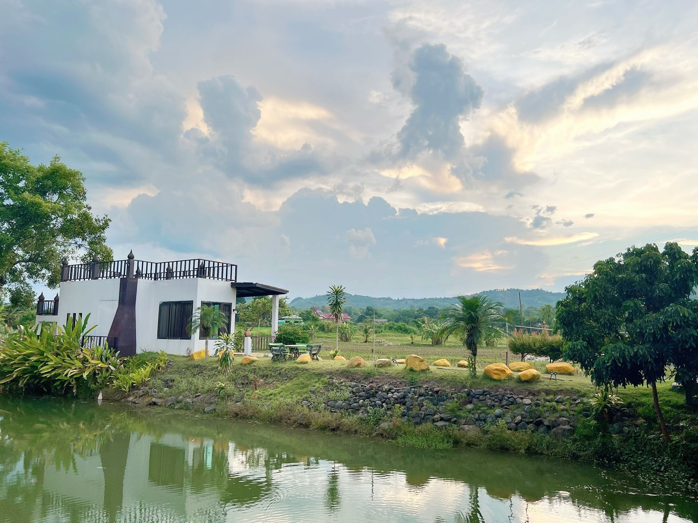 A modern house with a balcony, a pond, and surrounding greenery.