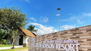 Schild für The Green Season Resort in Chiang Rai, mit modernem Design, einer Steinfassade und einem klaren Himmel im Hintergrund.