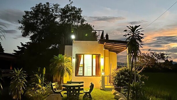 Ein modernes Haus mit gepflegtem Rasen, einer Terrasse mit Sitzgelegenheiten und Blick auf den Abendhimmel.