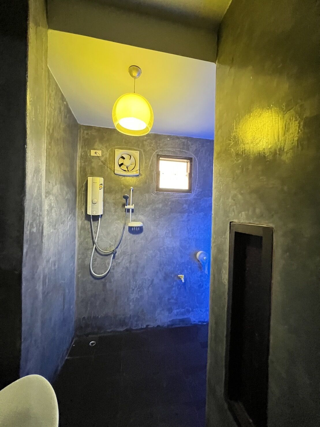 A compact bathroom with a shower, a small window, and a wall-mounted fan.