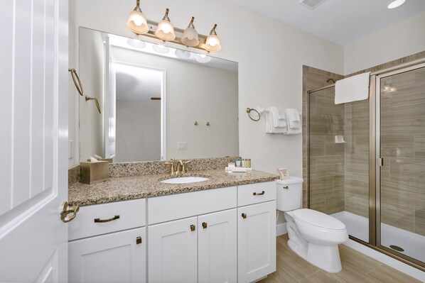 Un baño moderno con lavamanos de granito, un espejo grande y ducha con cerramiento de vidrio.