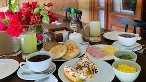 Una mesa de desayuno con diferentes alimentos, una taza de café, una botella de leche y un jarrón con flores.