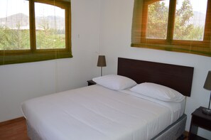 A single bed with a wooden headboard, two bedside tables with lamps, and two windows with blinds. - TukunMapu Hotel Boutique (Vicuña)
