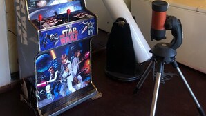 Un juego de arcade de Star Wars, un telescopio y un cartel con temática de Star Wars en una pared.