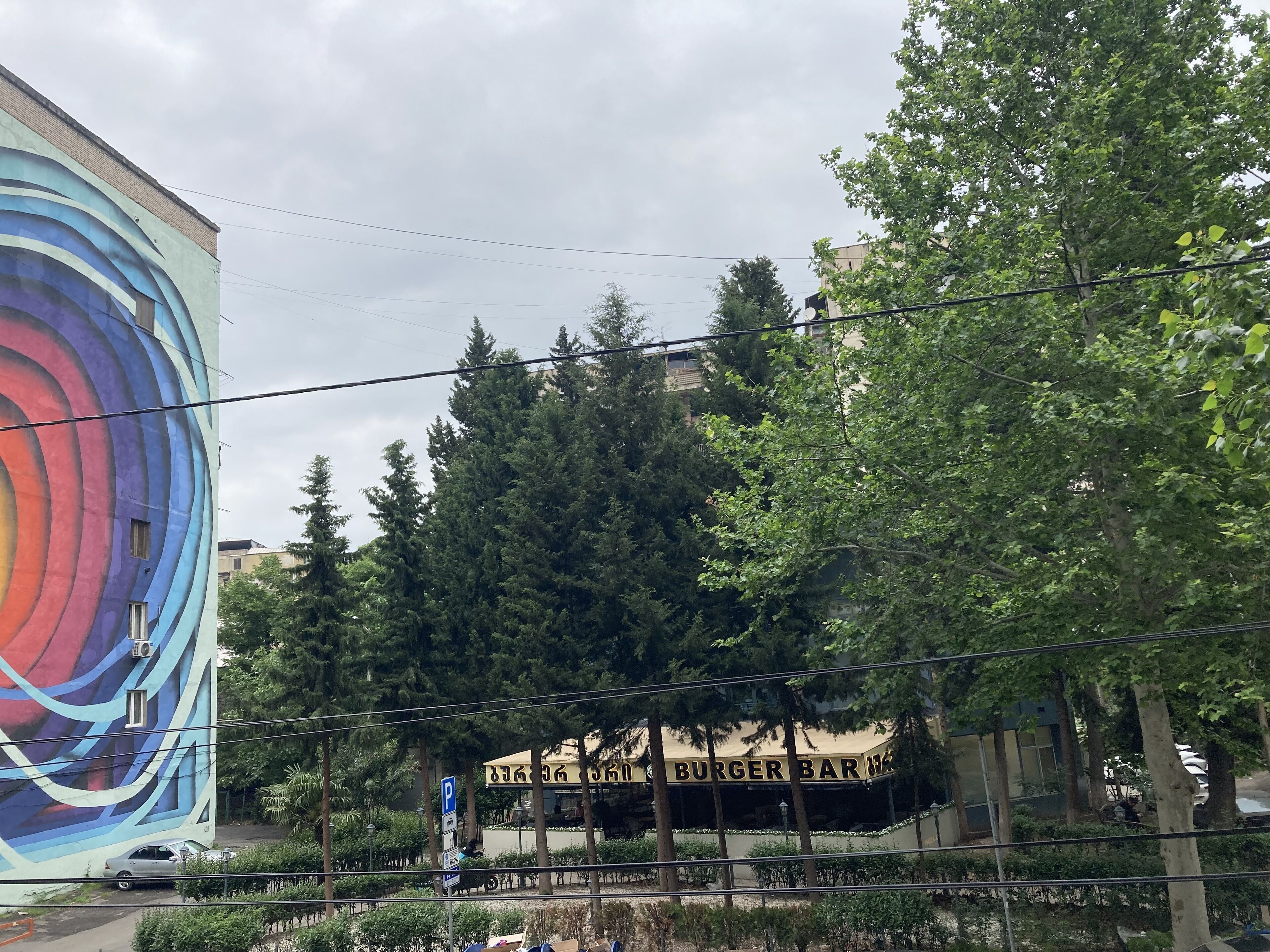 Un edificio con un mural colorido en una de sus fachadas y un letrero que anuncia una hamburguesería.