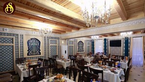 A dining area with multiple tables set for meals, featuring traditional patterned wall decorations and chandeliers. - Shohnishin Boutique  (Bukhara)