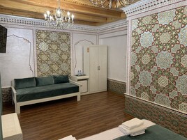 Una habitación con sofá verde, un armario, una mesita de noche con lámpara y una pared decorativa con diseños intrincados.