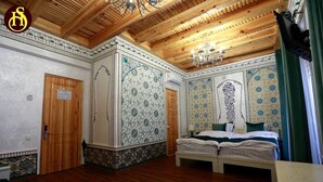 A room with a wooden ceiling, a bed with white bedding, and patterned walls. - Shohnishin Boutique  (Bukhara)