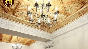 A hotel room with four beds, each with white linens and maroon throw pillows. A chandelier hangs from the ceiling, and the room has wooden paneling and a white textured wall. - Shohnishin Boutique  (Bukhara)