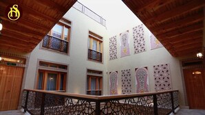 A courtyard with a wooden balcony railing, multiple windows with decorative patterns, and a brick building facade. - Shohnishin Boutique  (Bukhara)