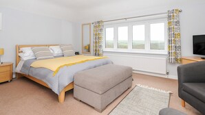 A bedroom with a bed, bedside table, TV, and a window with curtains. - Great Brightor Cob Barn (Bodmin)