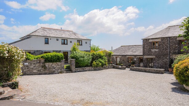 A courtyard with two stone buildings, one with a white facade and the other with a grey stone facade. - Great Brightor Cob Barn (Bodmin)