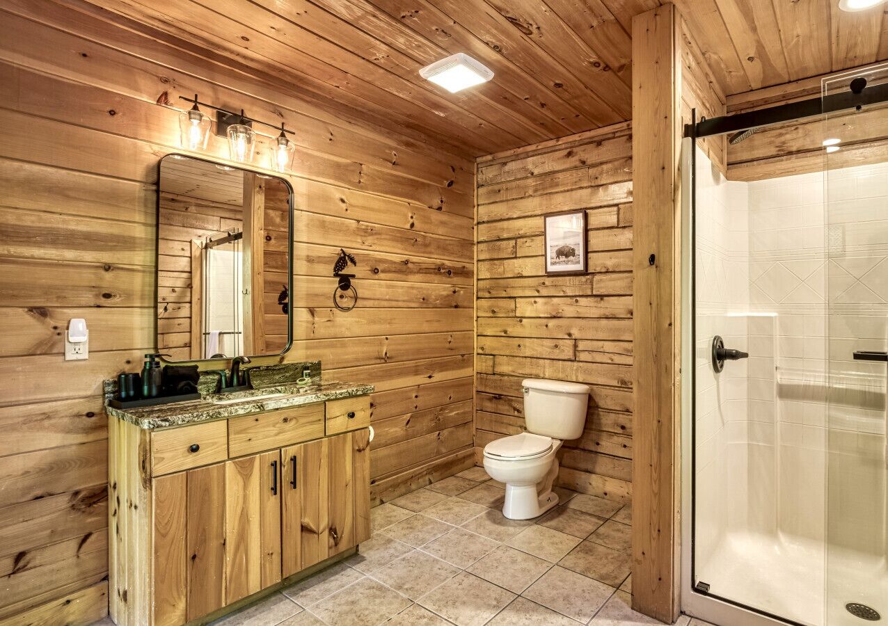 Ein Badezimmer einer Holzhütte mit einem Holztischchen, einer Toilette und einer Duschkabine aus Glas.