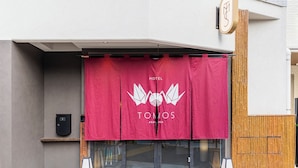 Entrada de hotel con toldo rojo que muestra el nombre y el logotipo del hotel.