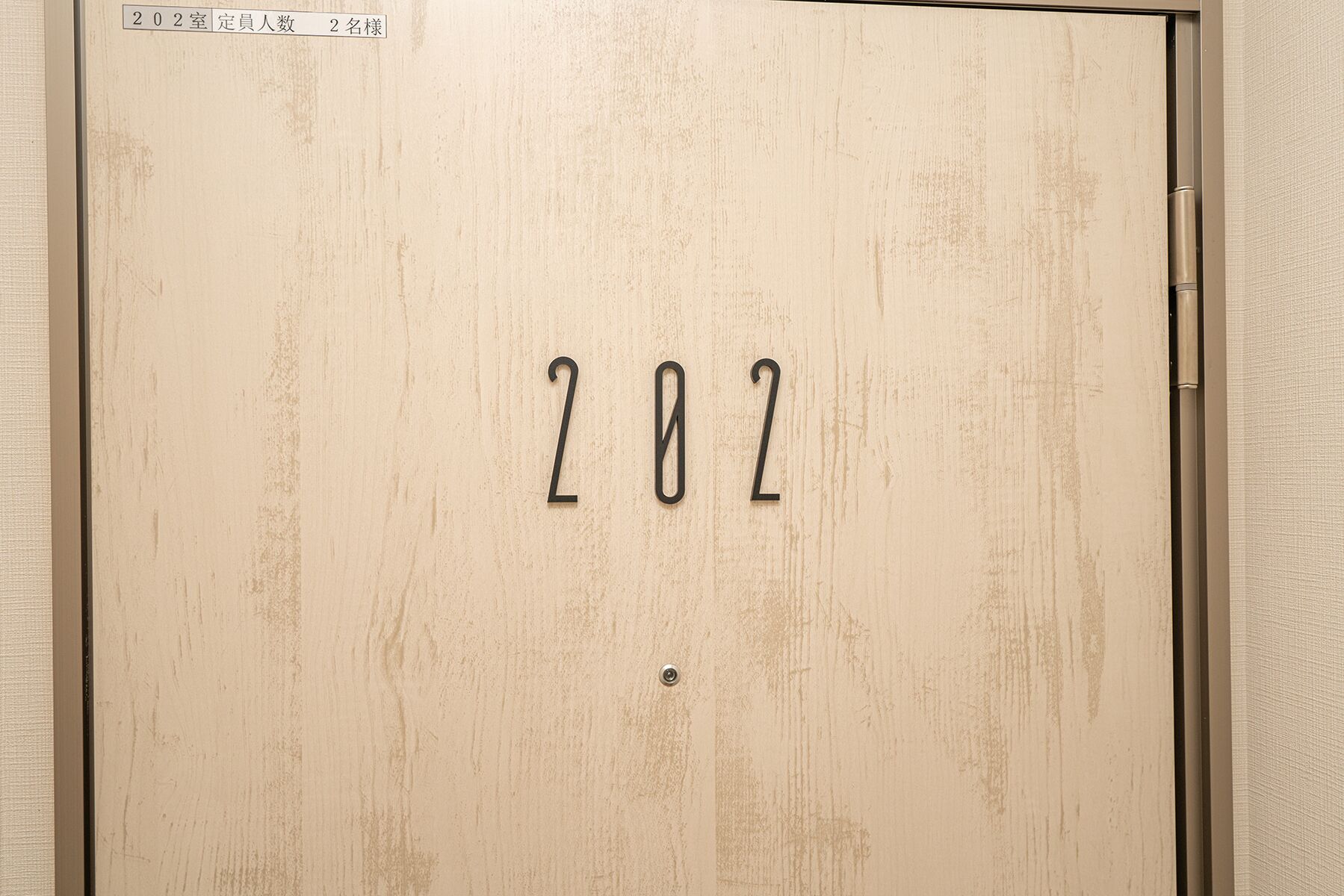 Eine Tür mit der Nummer 202 und einem Schild, das sie als Doppelzimmer für zwei Personen kennzeichnet.