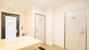 Um saguão de hotel com balcão de recepção, duas portas com números de quarto e um sinal de saída de emergência.