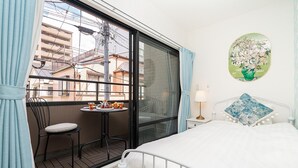 Quarto de hotel com varanda, uma cama, uma pequena mesa com xícaras de chá e uma obra de arte na parede.