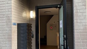 Entrada de hotel com fachada de tijolos, uma caixa de correio metálica e porta que dá acesso a uma escadaria.