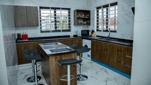 Una cocina moderna con una isla central, taburetes de bar, armarios de madera y un microondas.