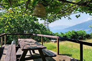 A wooden picnic table with benches, a hanging wicker basket, and a view of a mountainous landscape with a body of water. - Apartment 'Villa Adele' with Lake View, Private Pool and Wi-Fi (Segna)
